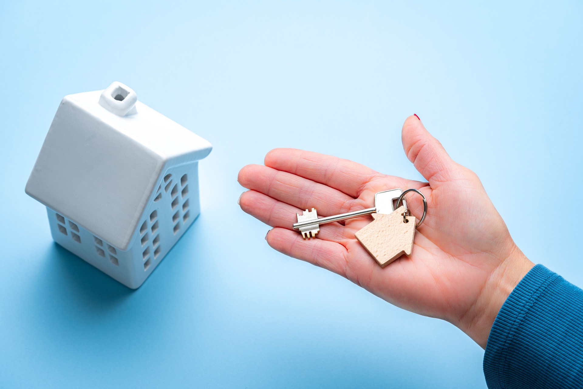 High angle view of hand holding new house key on blue background. Buying new house concept